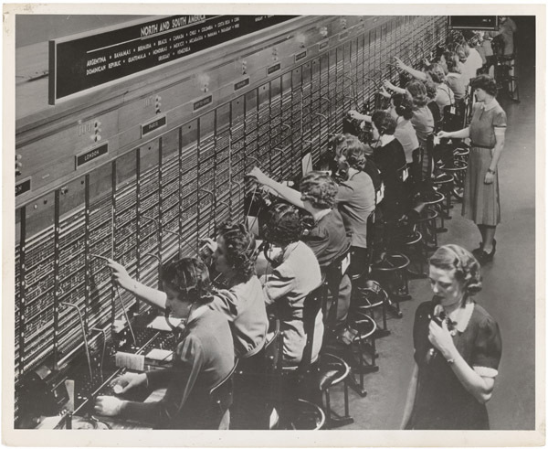 Black-and-white photo of telephone operators at a long Bell System switchboard, patching calls by hand